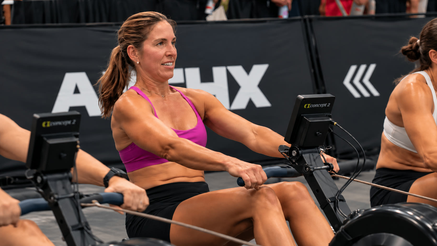 Andreina Carvallo rowing on an indoor rower during the endurance zone at ATHX Miami Beach, focused and smiling